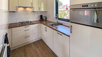 Une cuisine moderne avec des armoires blanches, un plan de travail en bois, un four encastré et une fenêtre donnant sur l’extérieur.