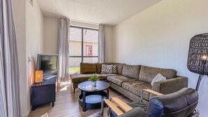 Ein modernes Wohnzimmer mit einem Ecksofa, einem Couchtisch, einem Fernseher und einer Lampe.