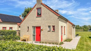 Ein Steinhaus mit roter Tür und Fenstern, einer Bank davor und einer Rasenfläche im Vordergrund.