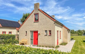 Un bâtiment en pierre avec une porte et des fenêtres rouges, un banc à l’extérieur et une pelouse devant.