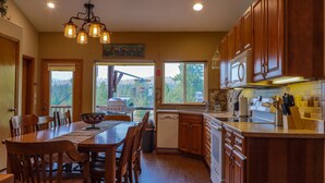 A spacious kitchen with wooden cabinets, a dining table, and a view of a backyard. - THE BIRDHOUSE,... Quiet Country Home in the Bitterroot Valley. (Florence)