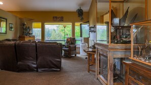 A living room with a sectional sofa, a wooden cabinet with glass doors, and a view of the outdoors. - THE BIRDHOUSE,... Quiet Country Home in the Bitterroot Valley. (Florence)