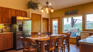 A kitchen with wooden cabinets, a stainless steel refrigerator, a dining table with chairs, and a hanging light fixture. - THE BIRDHOUSE,... Quiet Country Home in the Bitterroot Valley. (Florence)