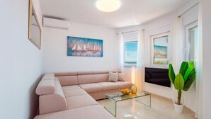 A modern living room with a beige sectional sofa, a glass coffee table, and a painting of sailboats. - 2 bedroom beach front apartment in Banjol (Banjol)