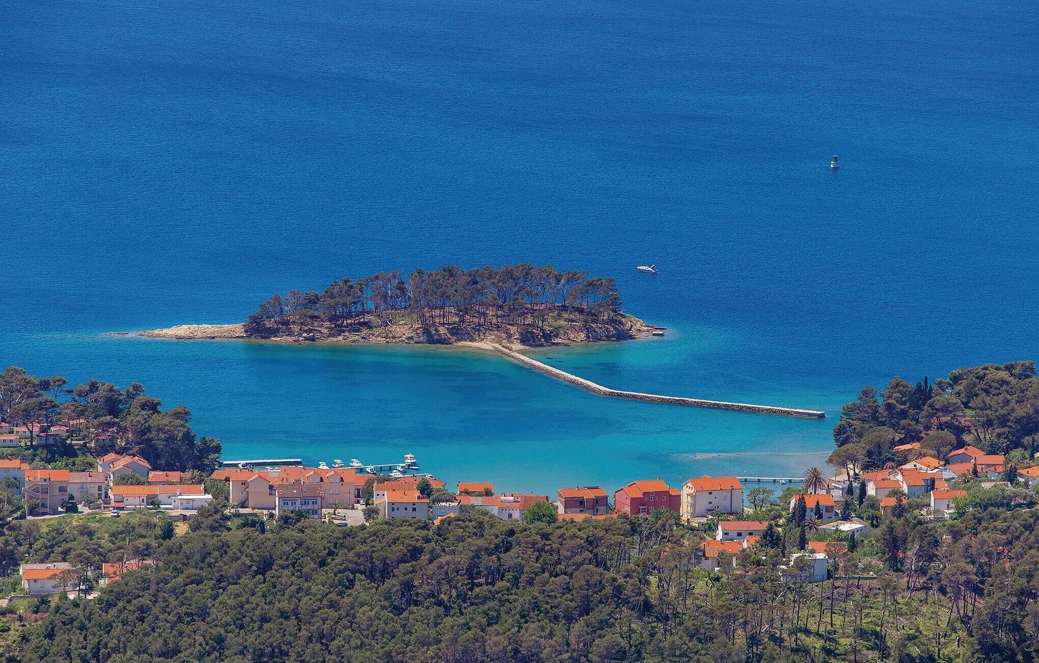 Vue aérienne d’une ville côtière avec une petite île, des eaux d’un bleu limpide et une jetée qui la relie au continent.