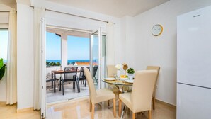 A modern dining area with a glass table, beige chairs, and a view of the sea through large windows. - 2 bedroom beach front apartment in Banjol (Banjol)