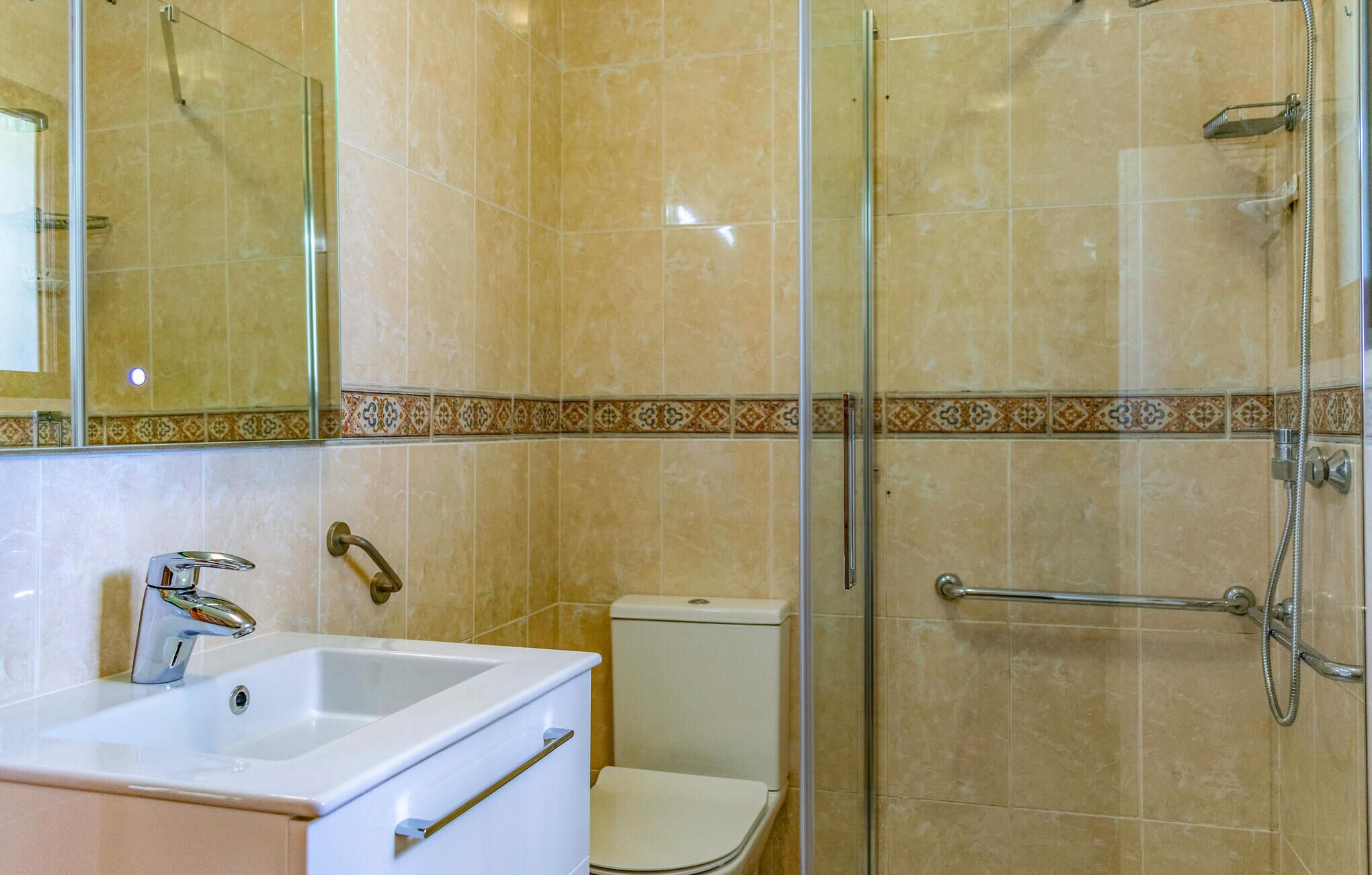 A bathroom with a glass shower enclosure, a toilet, and a sink with a mirror above.