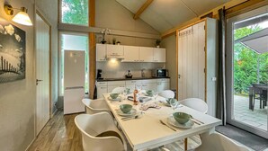 Cocina compacta con armarios blancos, una mesa de comedor preparada para cuatro comensales y vistas al exterior con vegetación.