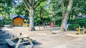 Un parque infantil con columpios, toboganes y estructuras para escalar, rodeado de árboles y una mesa de picnic.