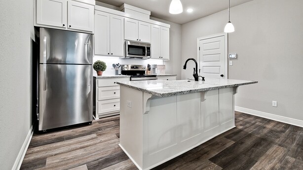A kitchen with white cabinets, a stainless steel refrigerator, a microwave, and a granite countertop island.