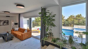 Un soggiorno moderno con un divano, un tavolino da caffè e una grande finestra vista piscina.