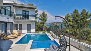 Una moderna casa a due piani con piscina, area salotto esterna e vista sul mare.