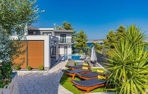 Una casa moderna a due piani con piscina, area relax esterna e vista sul mare.