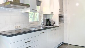 Une cuisine moderne avec des meubles blancs, un plan de travail en granit, un four encastré et une machine à café.