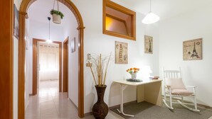 Un pasillo con una puerta de madera, un escritorio con una silla, un jarrón con flores y un cuadro de la Torre Eiffel.