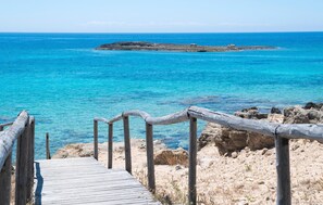 Una pasarela de madera que conduce a una costa rocosa con agua azul cristalina.