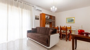 Una sala de estar con un sofá marrón, una mesa de comedor con sillas, una araña y un aparador con objetos decorativos.