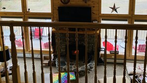 A room with a stone fireplace, wooden beams, and two deer heads mounted on the wall. - Spacious 3-Level Cabin Retreat-Sleeps 10, Wrap Around Deck, Peaceful and Private (Pittsburg)