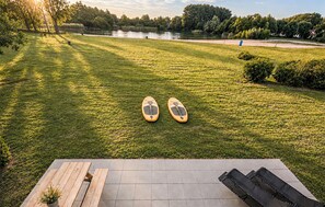 A grassy outdoor area with two paddleboards, a wooden bench, and a view of a lake and trees. - Gorgeous home in Ewijk (Ewijk)