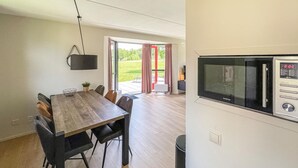Une cuisine moderne dotée d’un four à micro-ondes encastré, un coin repas avec une table et des chaises en bois, et une porte-fenêtre coulissante donnant sur une terrasse extérieure.