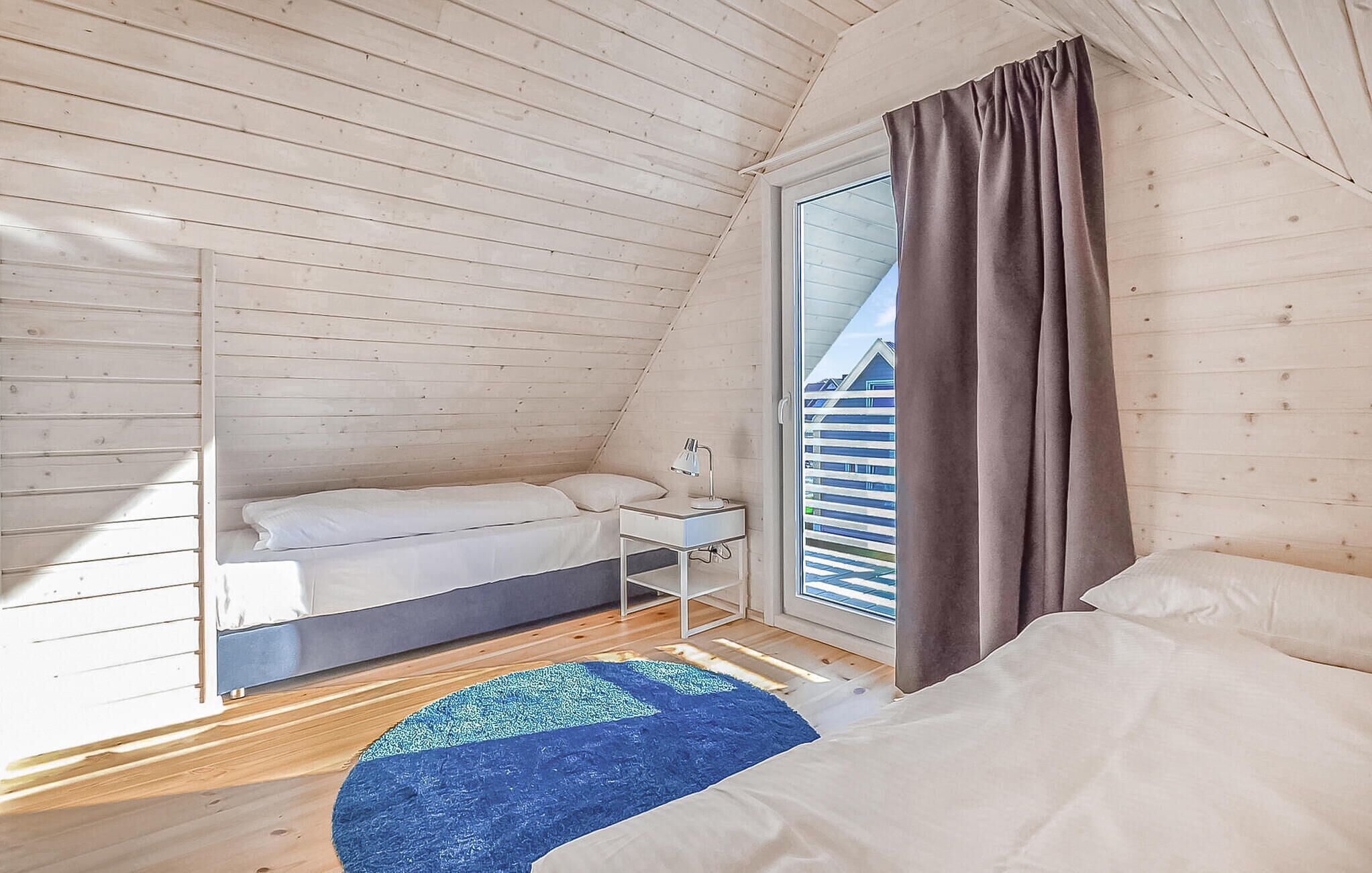 Un dormitorio pequeño y acogedor con techo inclinado, una cama, un escritorio con lámpara y una ventana con cortinas.