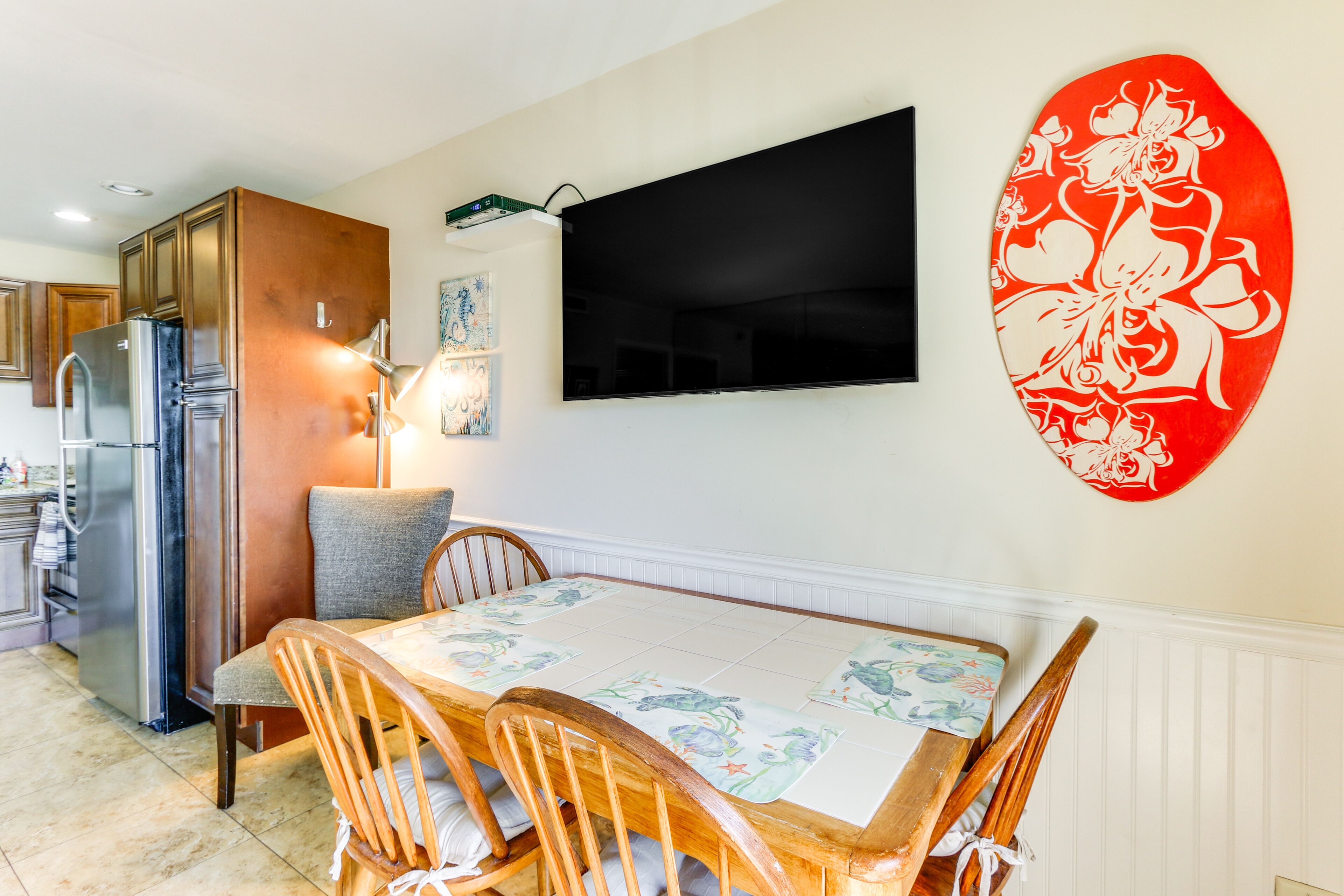 A dining area with a table, chairs, a flat-screen TV, and a decorative wall piece.