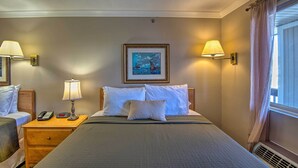 A hotel room with a large bed, two bedside tables with lamps, a painting on the wall, and a window with curtains.