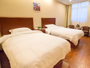 Une chambre d’hôtel avec deux lits, un plancher en bois, un tableau au mur, un bureau avec un téléphone et une plante, et une chaise près de la fenêtre.
