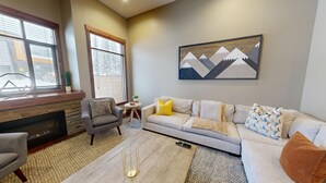A living room with a fireplace, a sofa, a chair, and a painting on the wall. - Luxury Townhouse in the Heart of Sun Peaks Village (Sun Peaks)