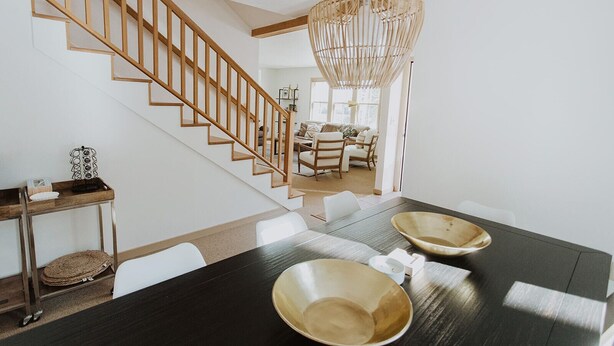 Un área de comedor moderna con una mesa de madera oscura, sillas blancas y una escalera de madera.