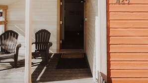 Un porche de madera con dos sillas Adirondack, una puerta oscura y el número 425 en la pared.