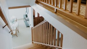 Una escalera de madera de varios niveles con barandilla, que lleva a una habitación con una silla blanca y una pequeña mesa.