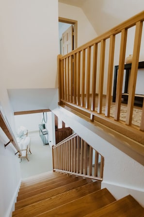 Staircase with handrails leads to a landing with a chair and table.