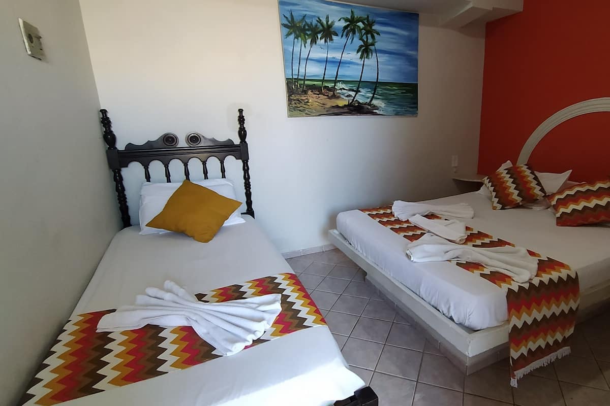 Une chambre avec deux lits, l’un doté d’une tête de lit en bois et l’autre d’une tête de lit incurvée. Un tableau représentant une scène de plage est accroché au mur, au-dessus des lits.