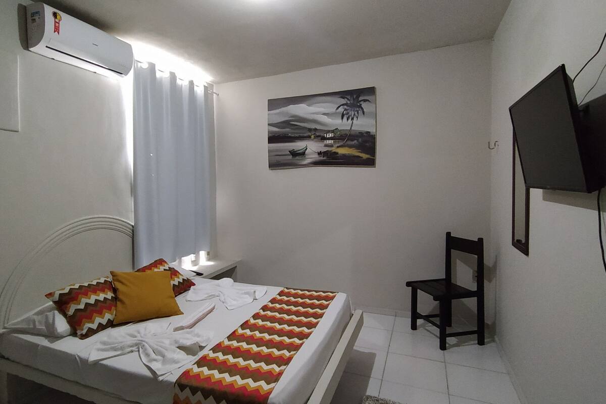 Une chambre à coucher avec un lit, une chaise, un téléviseur fixé au mur et un tableau accroché au mur.