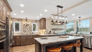 Une cuisine moderne avec des meubles en bois, des appareils en acier inoxydable, un grand îlot central doté de tabourets et un éclairage suspendu.
