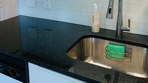 Een keuken met witte kasten, een roestvrijstalen spoelbak, een zwart aanrecht en een groene afwasschaal.