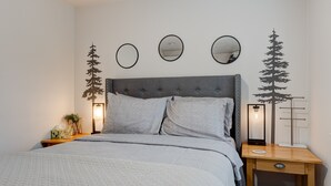 Quarto bem arrumado com cama, mesas de cabeceira e decorações nas paredes, incluindo espelhos e silhuetas de árvores.