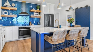 Una cocina moderna con una isla grande, gabinetes blancos, salpicadero azul y luces colgantes.