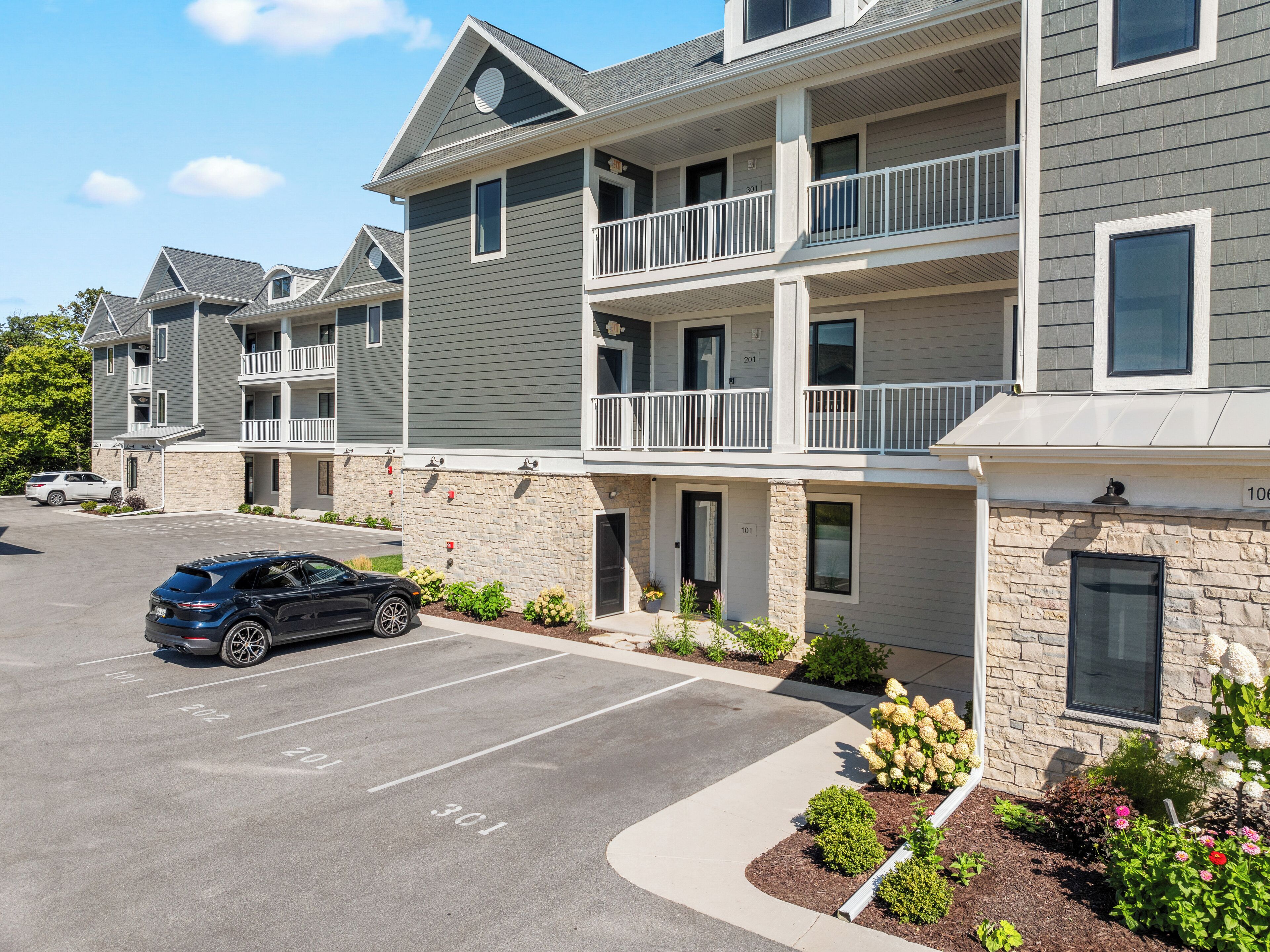 A multi-story apartment building with balconies, a parking lot, and landscaped gardens.