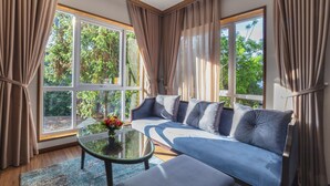 A modern living room with a blue sofa, a glass coffee table, and a vase of flowers. - Marigold Hotel Dalat (Xuan Huong - Da Lat)