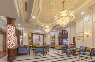 Un lobby lujoso con candelabros ornamentados, asientos mullidos y una obra de arte grande enmarcada en la pared.