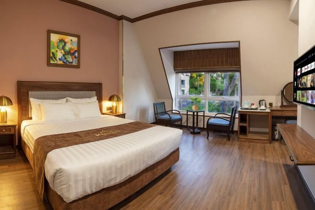 A hotel room with a large bed, a desk, a chair, and a TV.