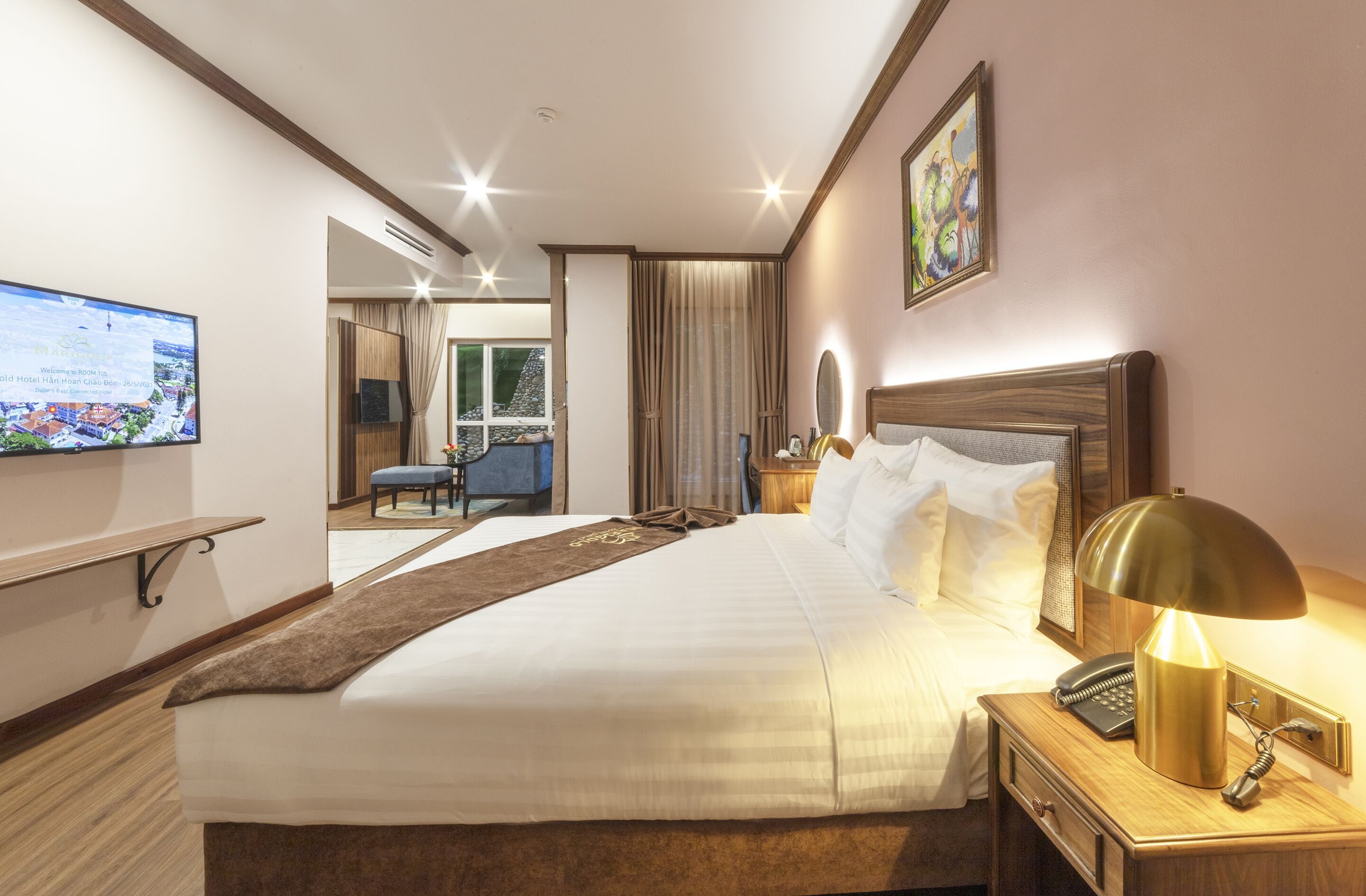 A hotel room with a large bed, a bedside table with a lamp, a TV mounted on the wall, and a view of the outside.