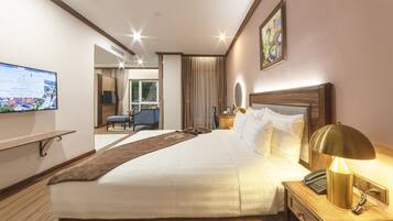 A hotel room with a large bed, a bedside table with a lamp, a TV mounted on the wall, and a view of the outside.