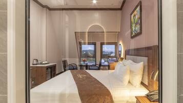 A hotel room with a large bed, a desk, a chair, and a view of the cityscape through the window.