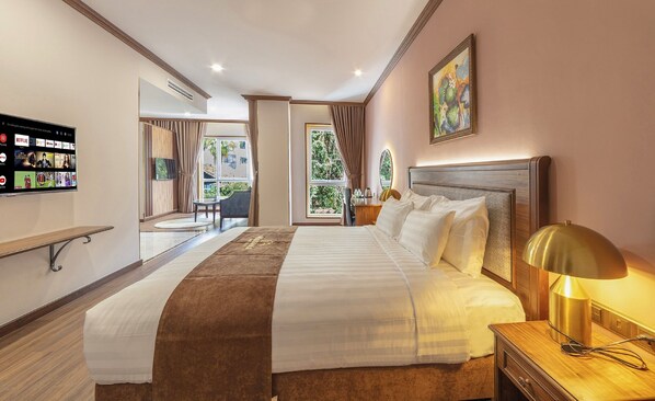 A hotel room with a large bed, a desk with a chair, a TV mounted on the wall, and a window with curtains.