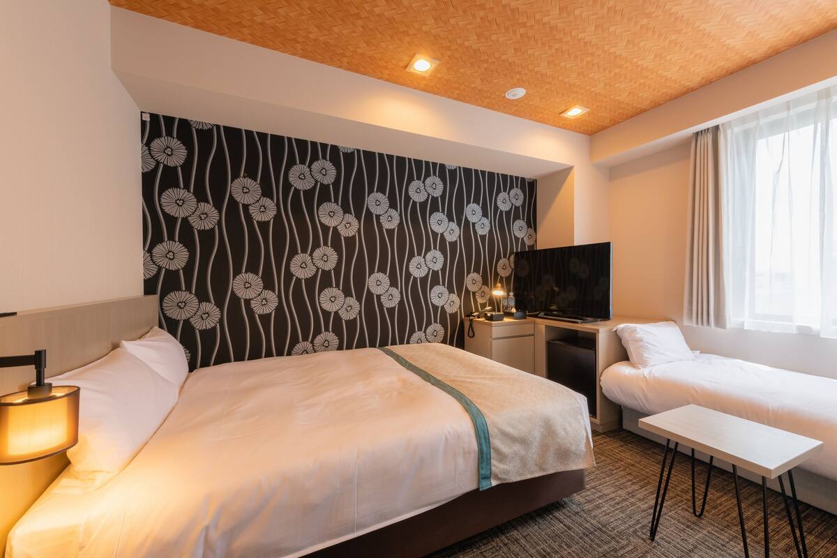 Una habitación de hotel con una cama grande, otra más pequeña, un escritorio y un televisor.