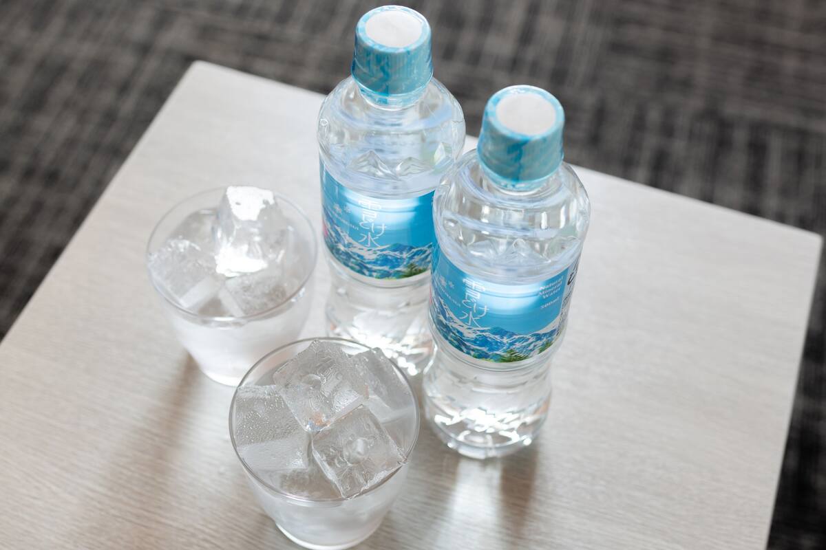 Tres botellas de agua cristalina y dos vasos con hielo sobre una superficie de madera.
