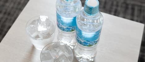 Three clear water bottles and two glasses with ice on a wooden surface.
